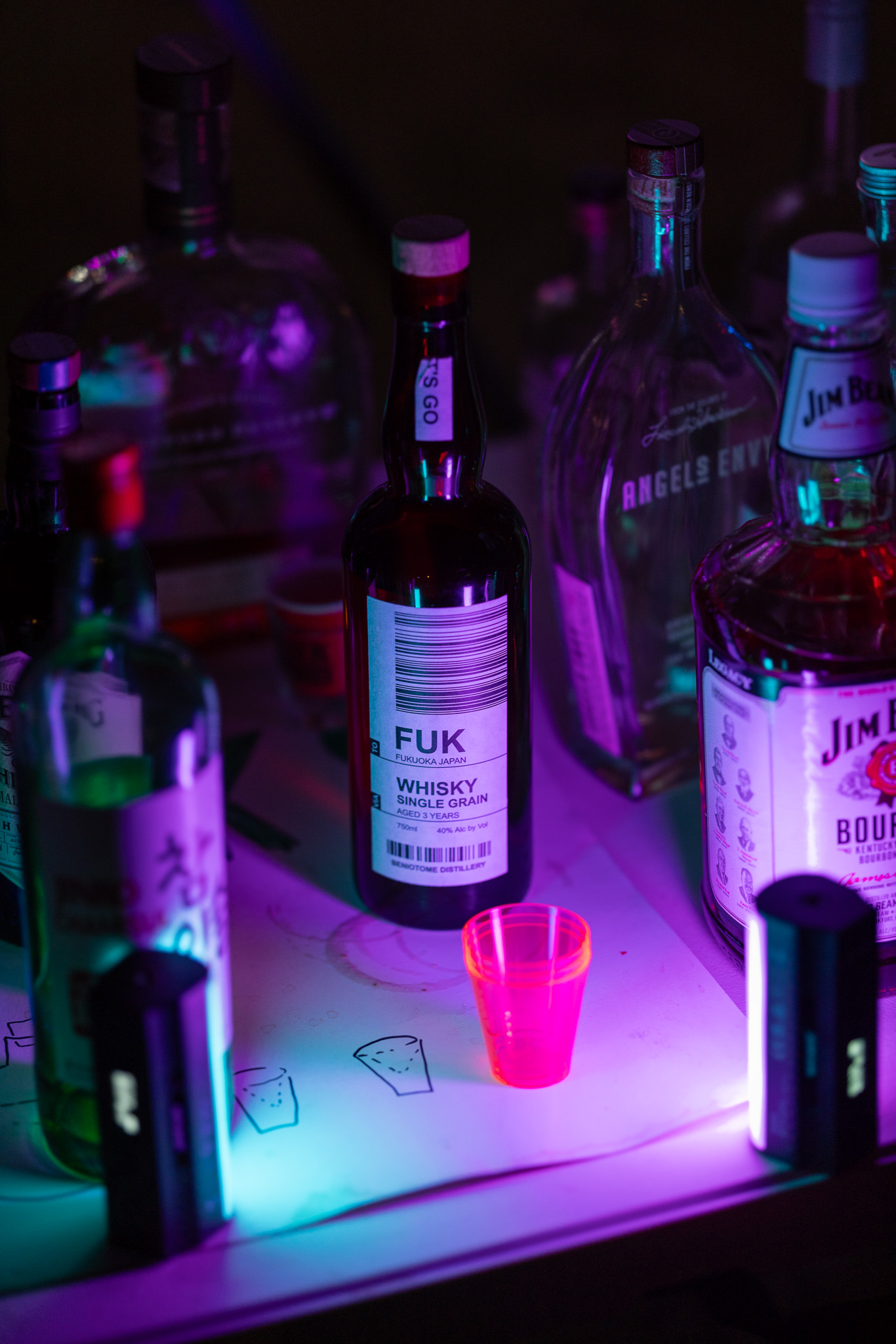 a bottle of 'FUK' Fukuoka whisky, lit by blue and pink LEDs on a table in front of it